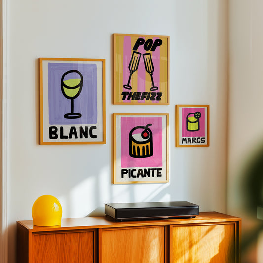 Colorful cocktail drinks posters on a wall above a wooden cabinet with a yellow vase and black device.