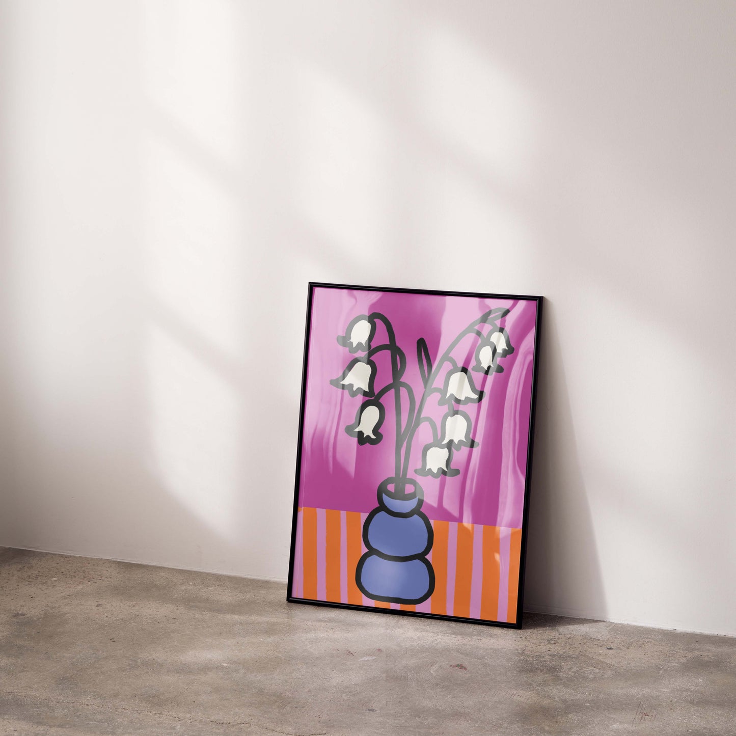 Framed artwork of a floral design on a pink background leaning against a white wall.
