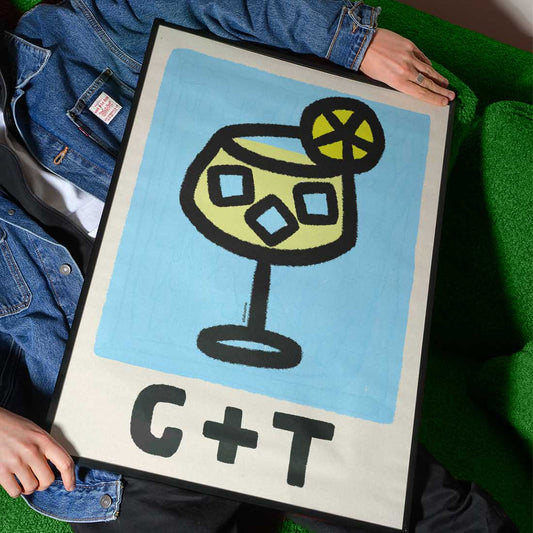 Person holding a framed artwork of a stylized cocktail with 'G+T' text on a green surface.