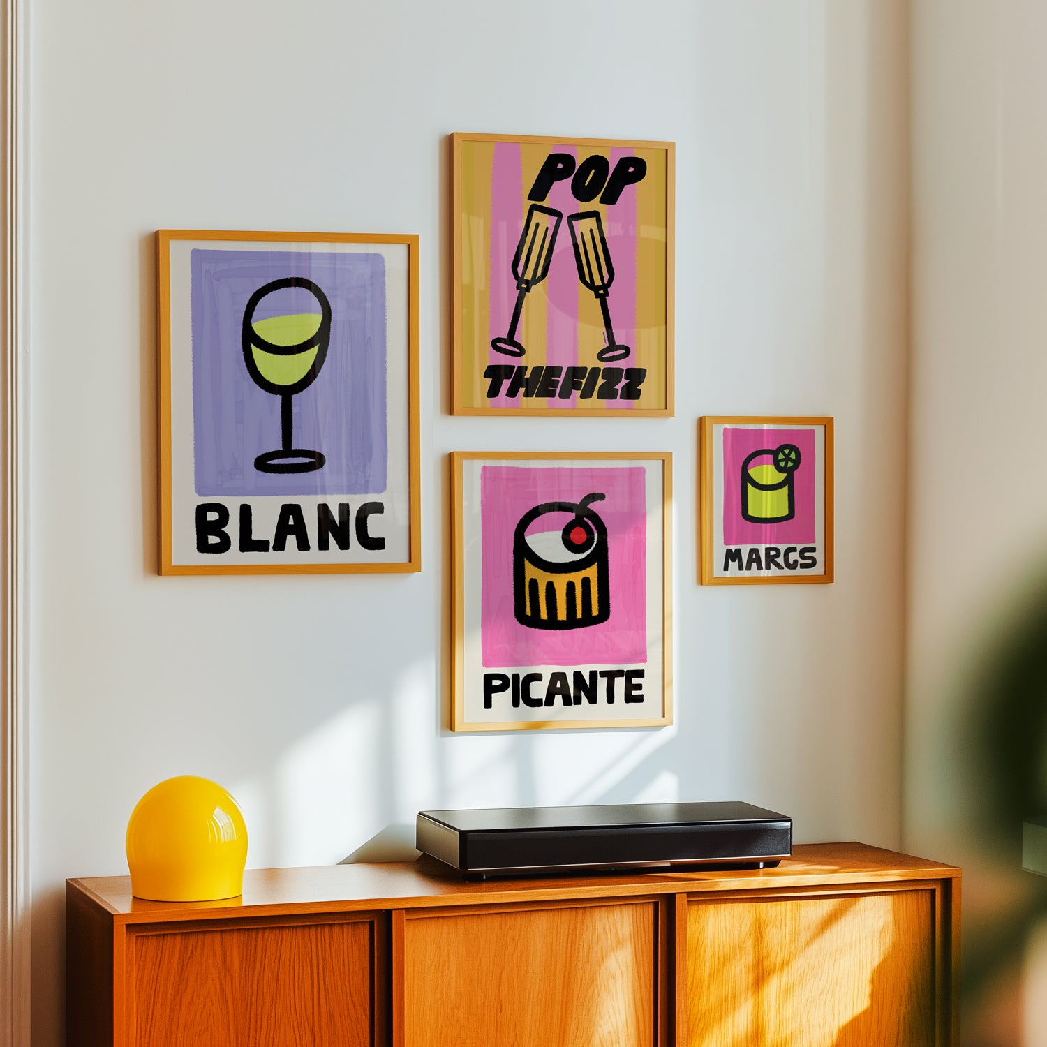 Colorful cocktail drinks posters on a wall above a wooden cabinet with a yellow vase and black device.