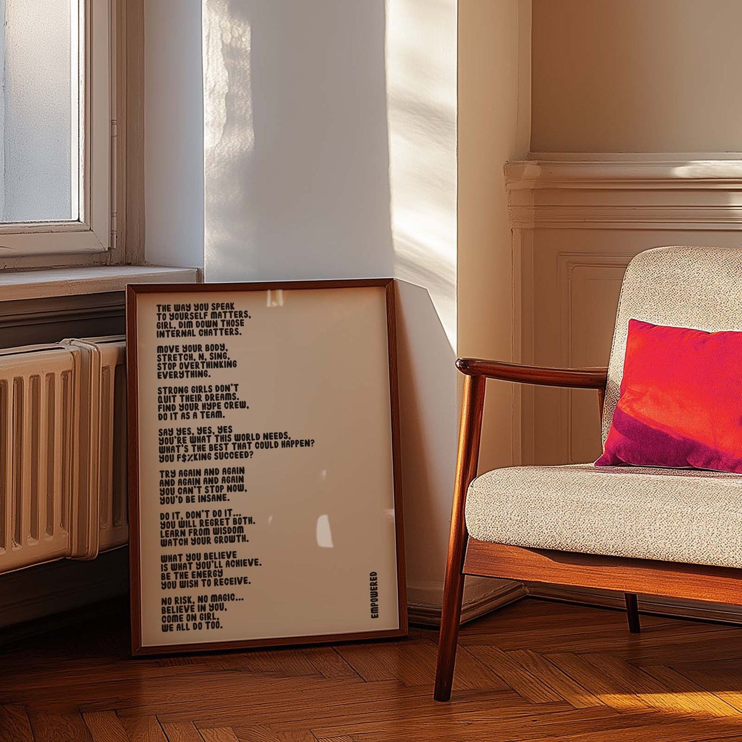 Framed  Typography-based art print featuring an empowering poem about strength and mindset, leaning against a wall next to a chair with a red pillow.