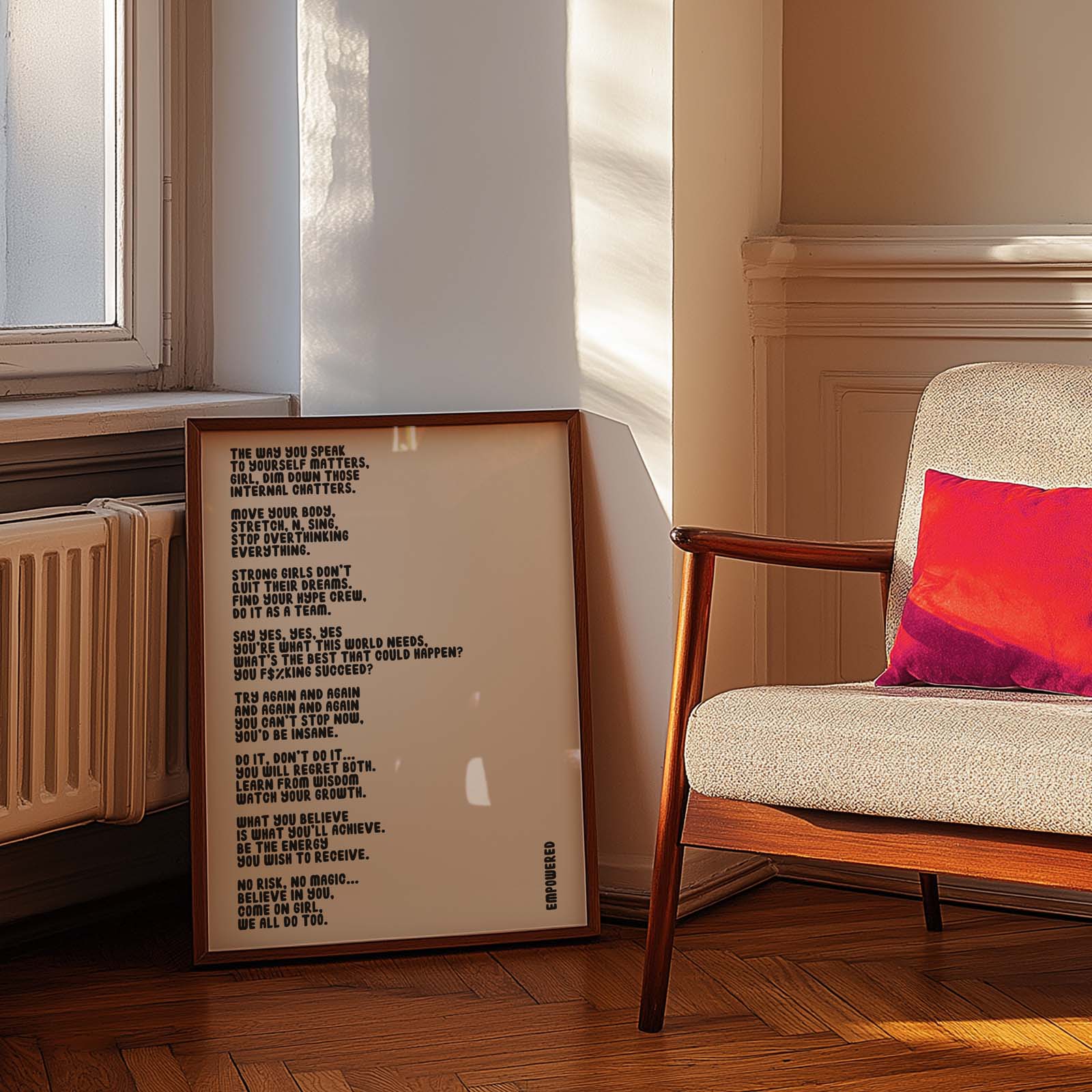 Framed  Typography-based art print featuring an empowering poem about strength and mindset, leaning against a wall next to a chair with a red pillow.