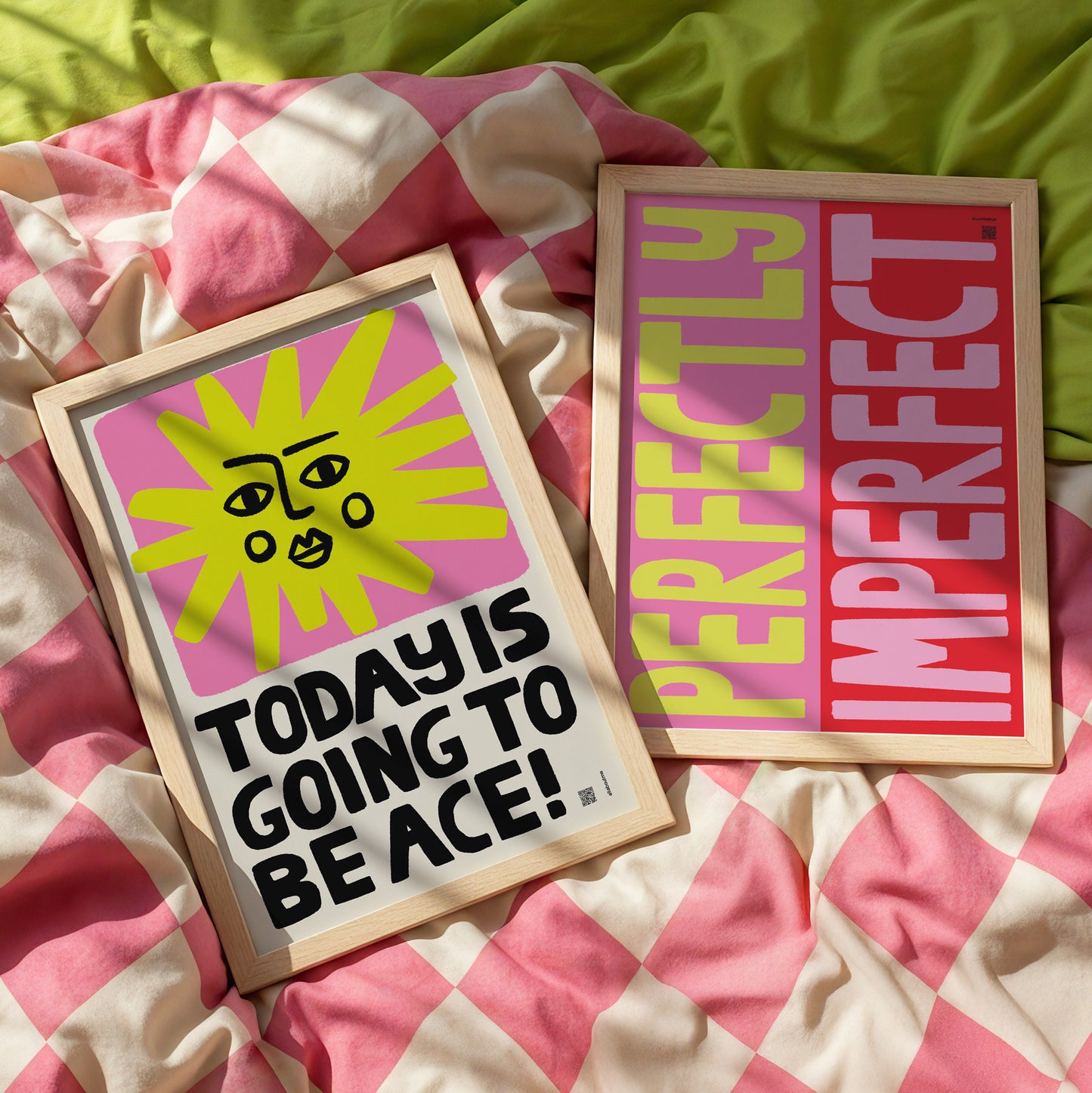Two framed prints on a checkered fabric background, one with a sun design and text, the other with 'Perfectly Imperfect' text.
