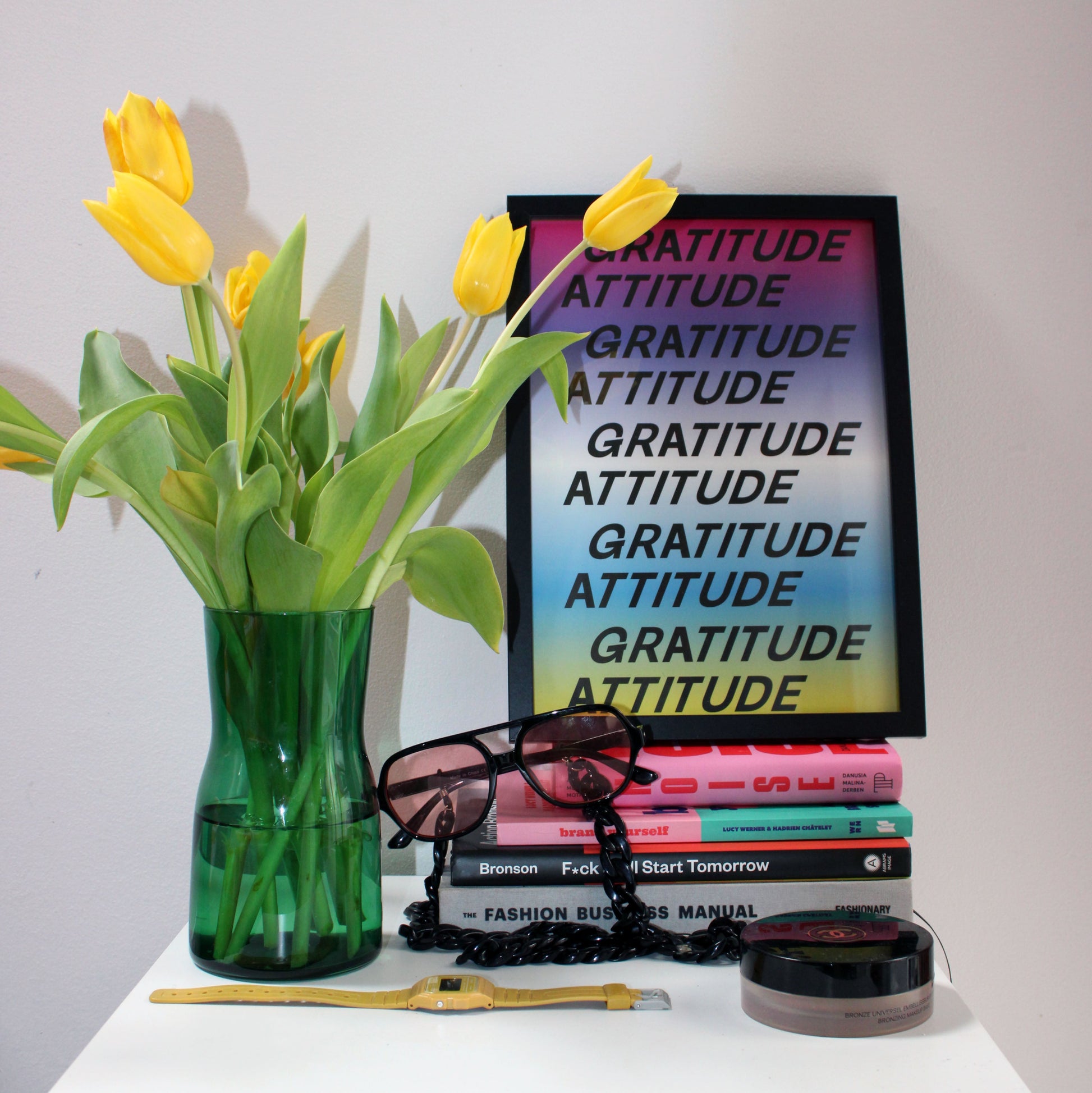Framed 'Gratitude Attitude' poster with yellow tulips and books on a white surface in bedroom for daily reminder.