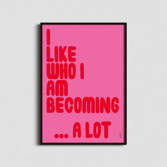 Framed poster with motivational quote 'I LIKE WHO I AM BECOMING... A LOT' on a pink background