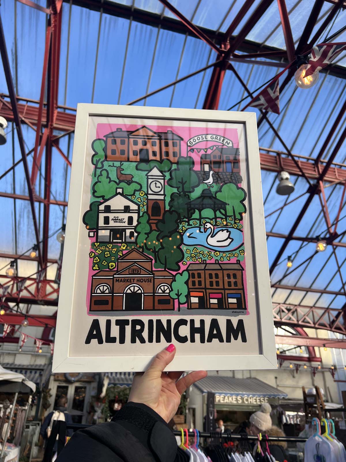 Poster of Altrincham held up in front of a Altricham market with a metal roof.