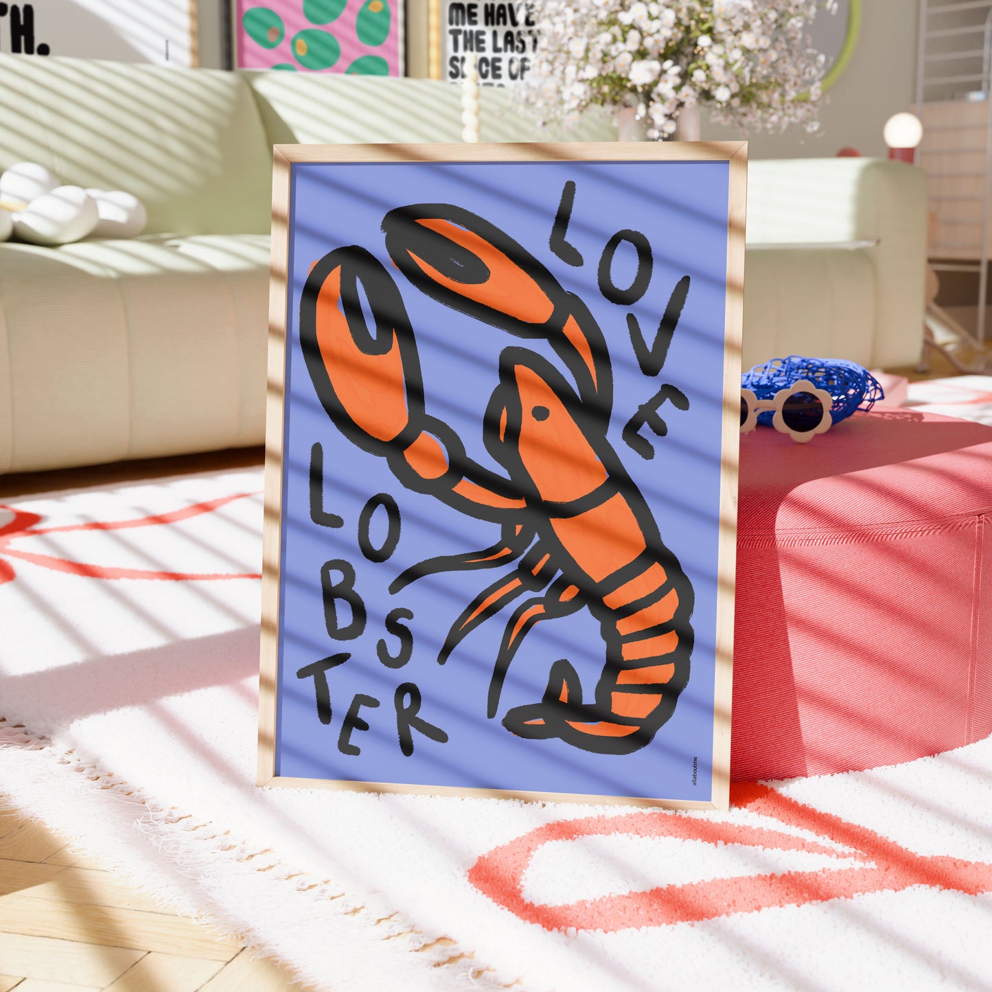 Framed artwork of a lobster with 'LOVE LOBSTER' text on a blue background, placed on a table in a room.