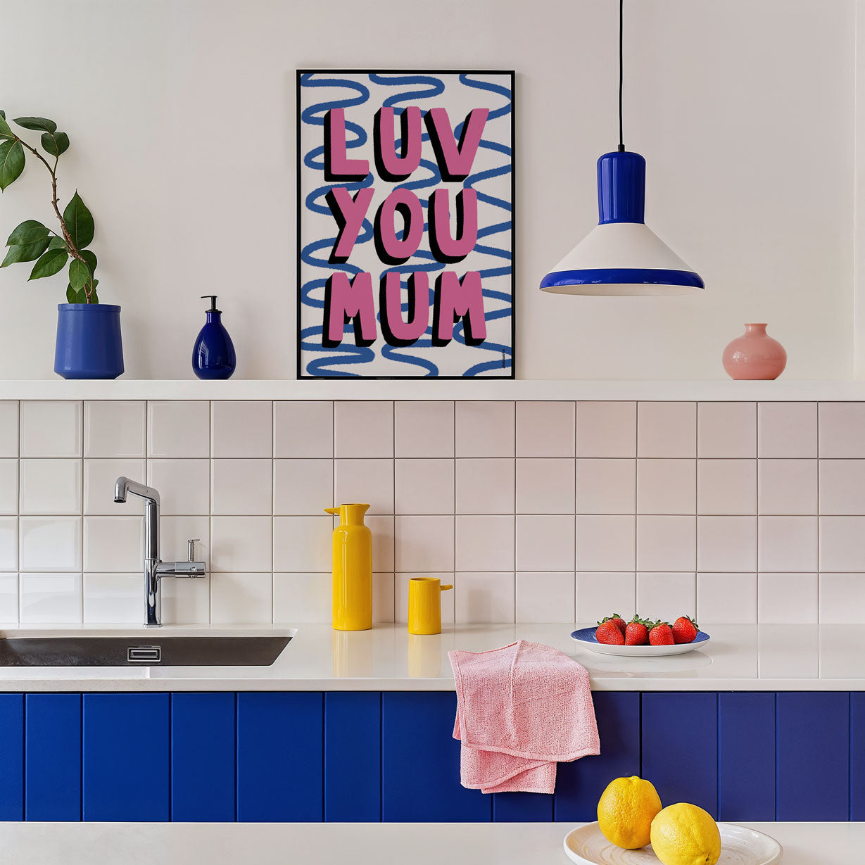 Modern kitchen with blue cabinets, white tiled wall, and colourful Luv you mum art print decor.