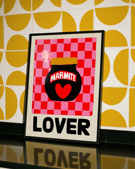 Framed artwork with a checkered pattern, jar of marmite design, and the word 'LOVER' on a yellow and white patterned wall.