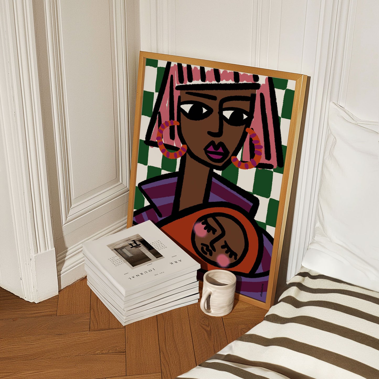 Framed abstract art of a woman with pink hair on a wooden floor next to books and a mug.