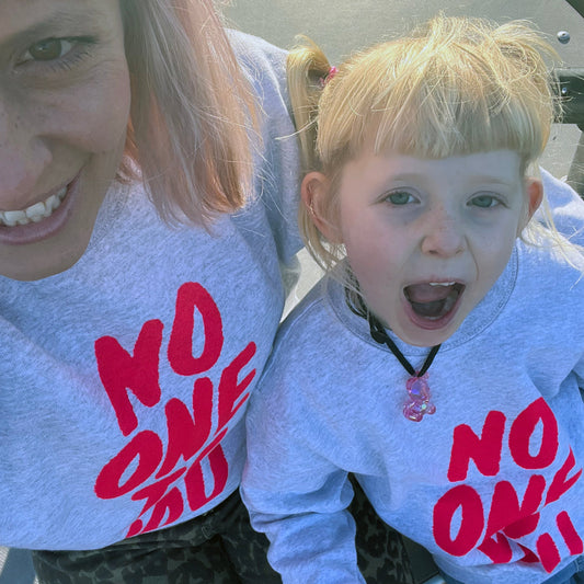 Mother and daughter wearing grey sweatshirts with 'NO ONE' printed in red.
