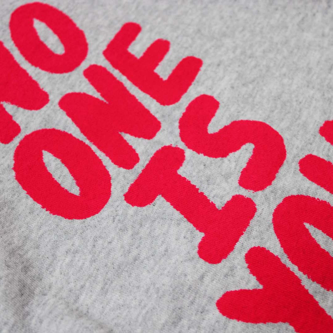 Gray sweatshirt with red text 'NO ONE IS YOU' on a textured fabric background