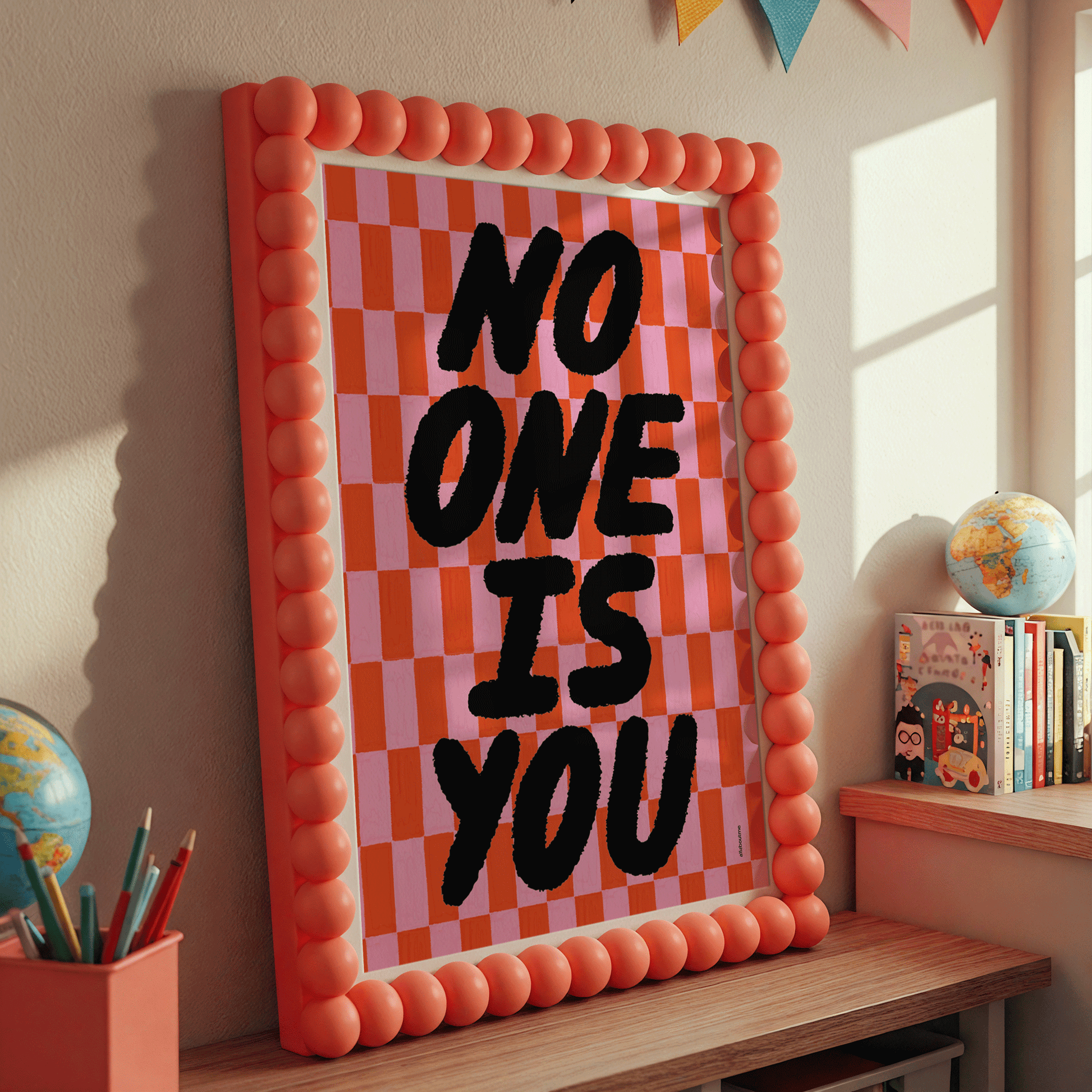 Decorative frame with 'No One Is You' affirmation text in a room with books and globes.