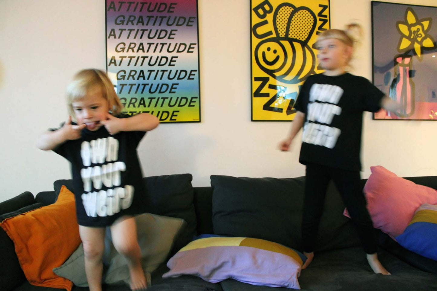 Two children in a living room with colorful pillows and wall art.