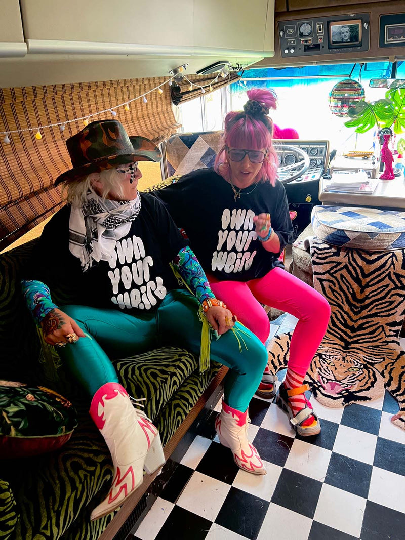 Lu in Luland, AKA Lou Featherstone wearing own your weird tshirt with designer Carla, sitting inside Susie with a checkered floor and colourful interior.