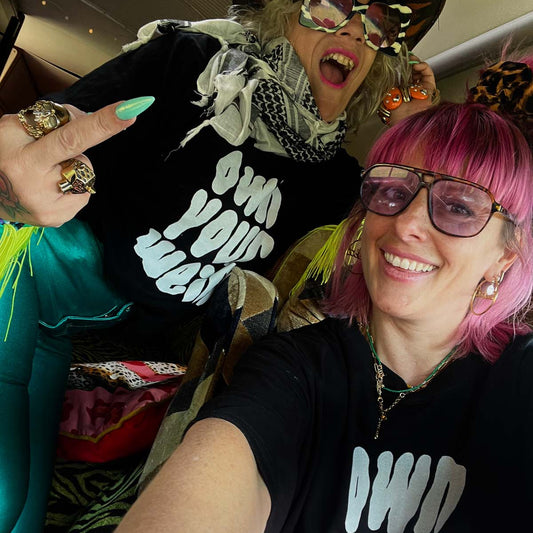 Lu in Luland, AKA Lou Featherstone wearing black, own your weird tshirt with designer Carla, sitting inside Susie with a checkered floor and colourful interior.