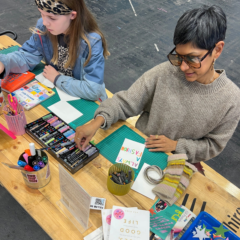 Two people working at a table with art supplies and materials making self love affirmation art.