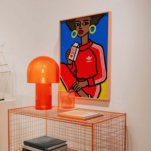 Orange lamp and decor items on a wire shelf with a colorful framed artwork of a person wearing an Adidas tracksuit.