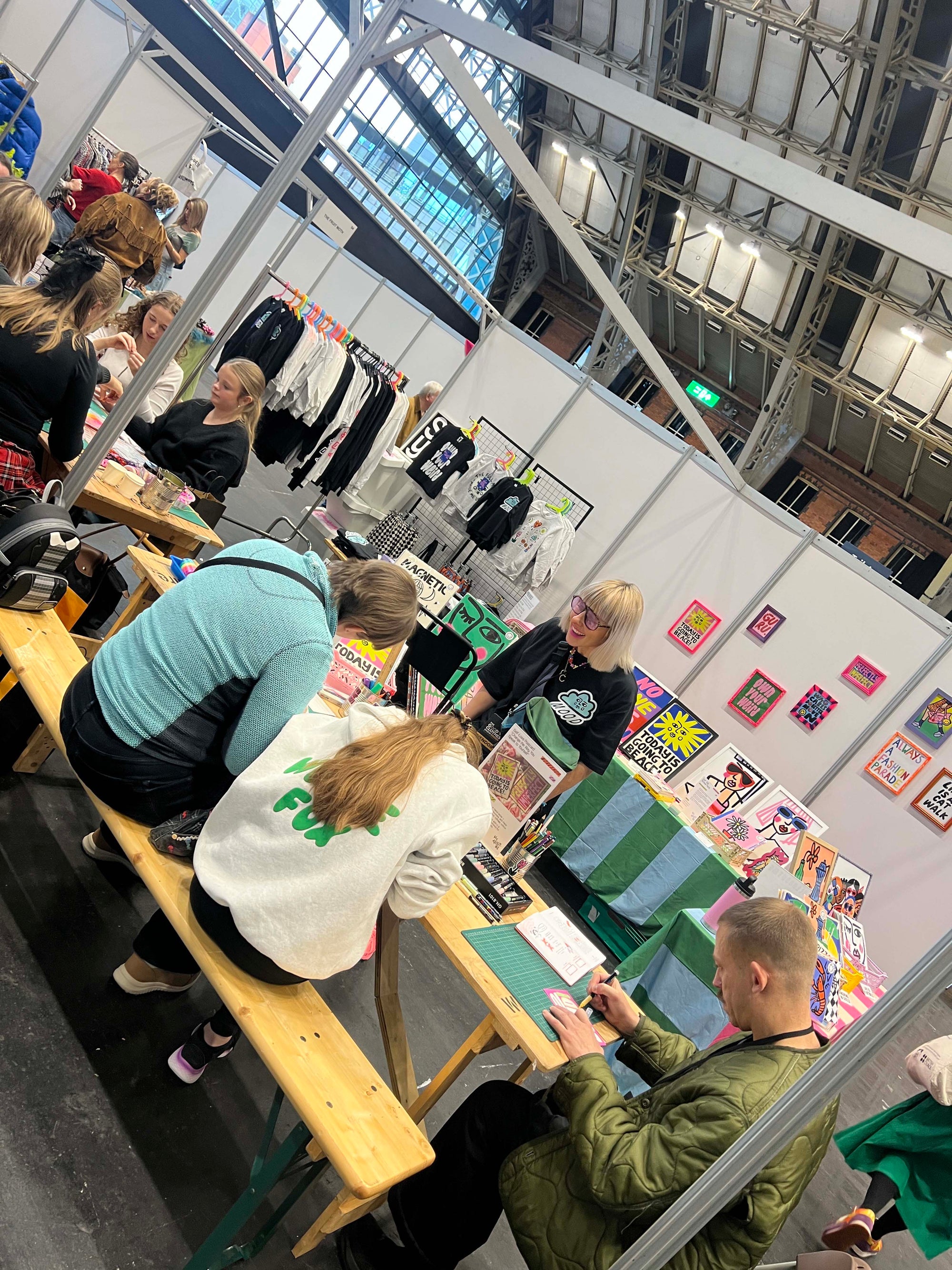 People interacting at a creative wellbeing workshop with various items on display in a large indoor venue.