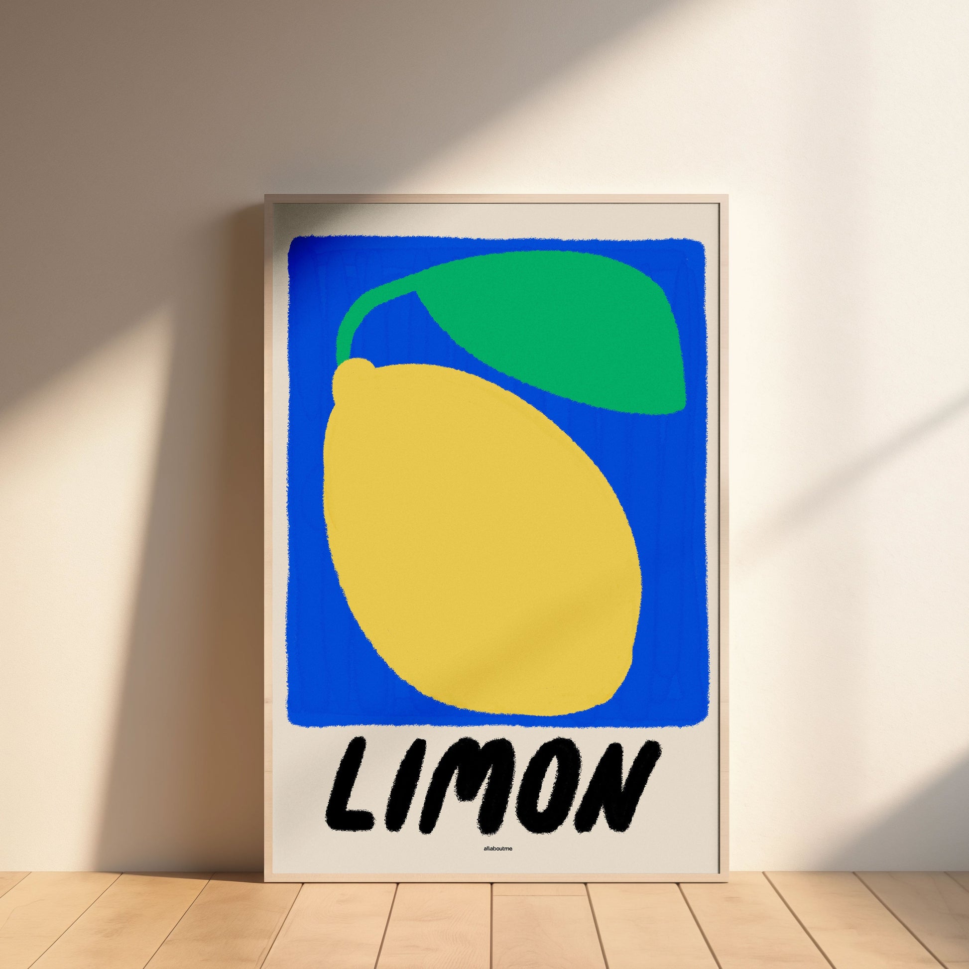 Framed artwork of a lemon with a green leaf and 'Limon' text on a blue background, leaning against a wall.