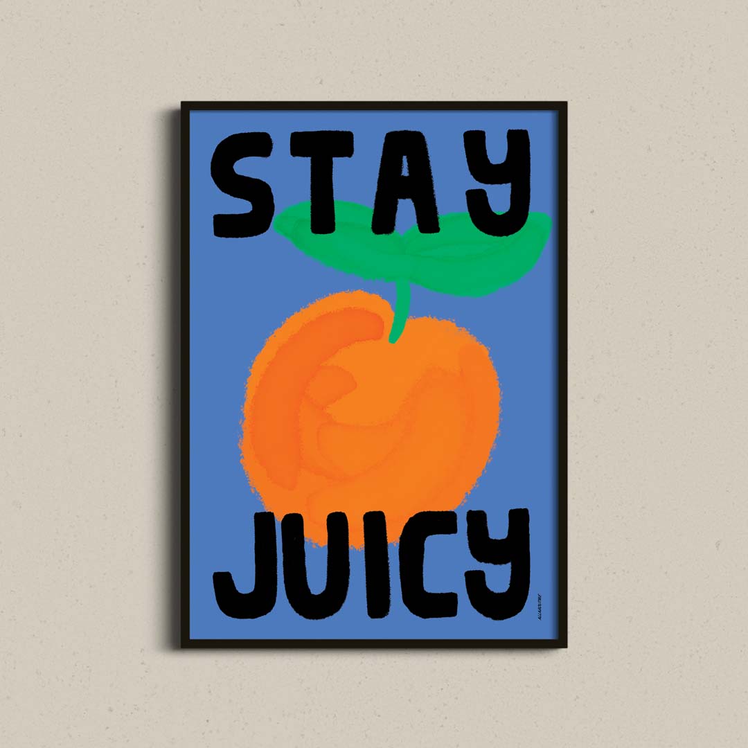 A framed poster featuring a stylized orange on a blue background with the words 'STAY JUICY' in bold black letters, displayed against a light beige textured wall.