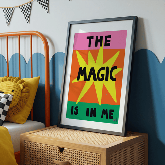 Framed poster with 'The Magic is in Me' text in a colorful design, placed on a wooden shelf in a room with a bed and decorative pillows.