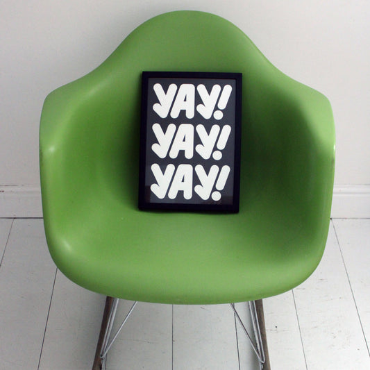 Green chair with a black frame displaying 'YAY! YAY! YAY!' on a white floor and wall.