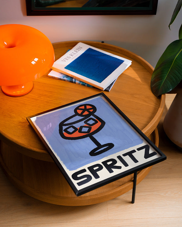 Table with a 'Aperol Spritz' sign, orange lamp, and plant in a room setting