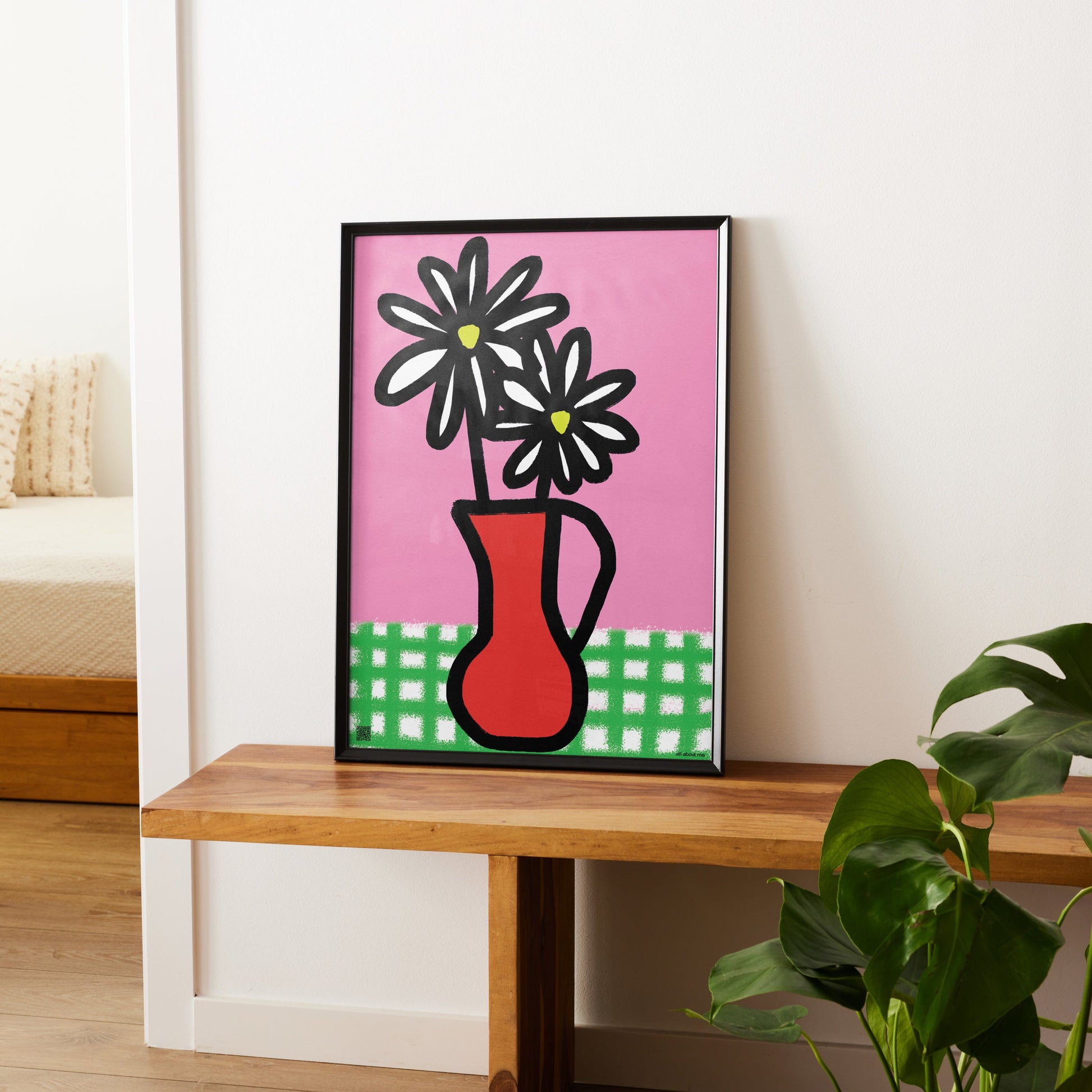 Framed Daisy birth flower artwork of a red vase with black flowers on a pink background, placed on a wooden shelf.