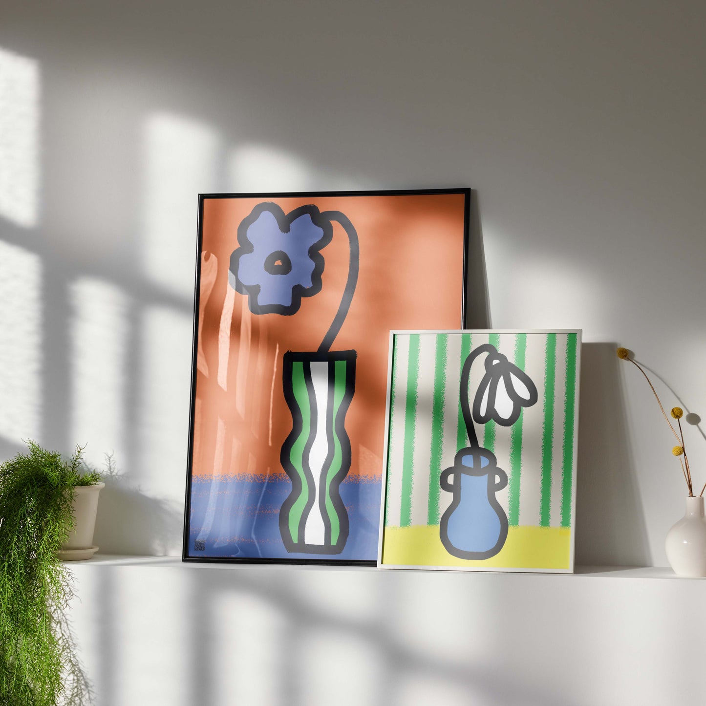Two abstract art prints on a shelf with decorative vases and plants.