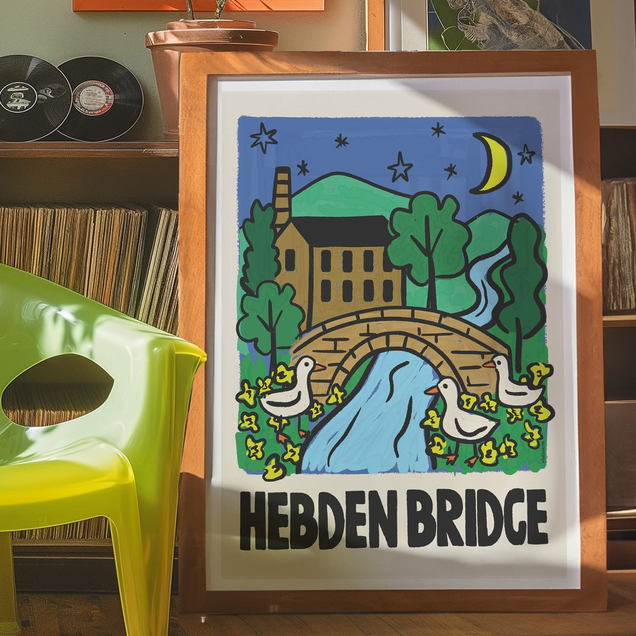 Framed artwork of Hebden Bridge with a green chair and records in the background
