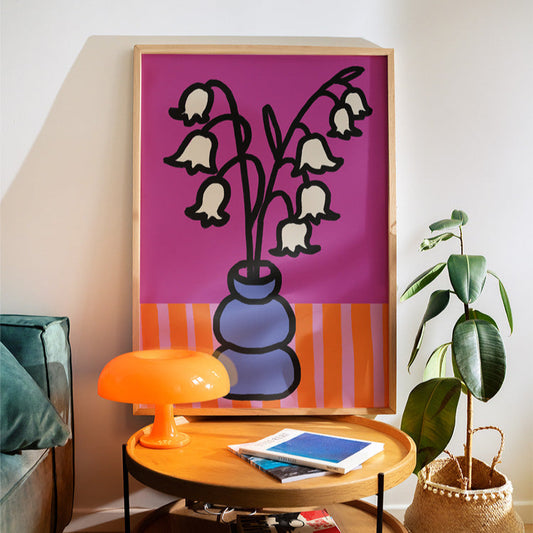Graceful Lily of the Valley art print for May birthdays. A timeless botanical illustration symbolising sweetness and new beginnings.
Decorative table with books, a lamp, and a plant in a room with a colorful abstract painting on the wall.