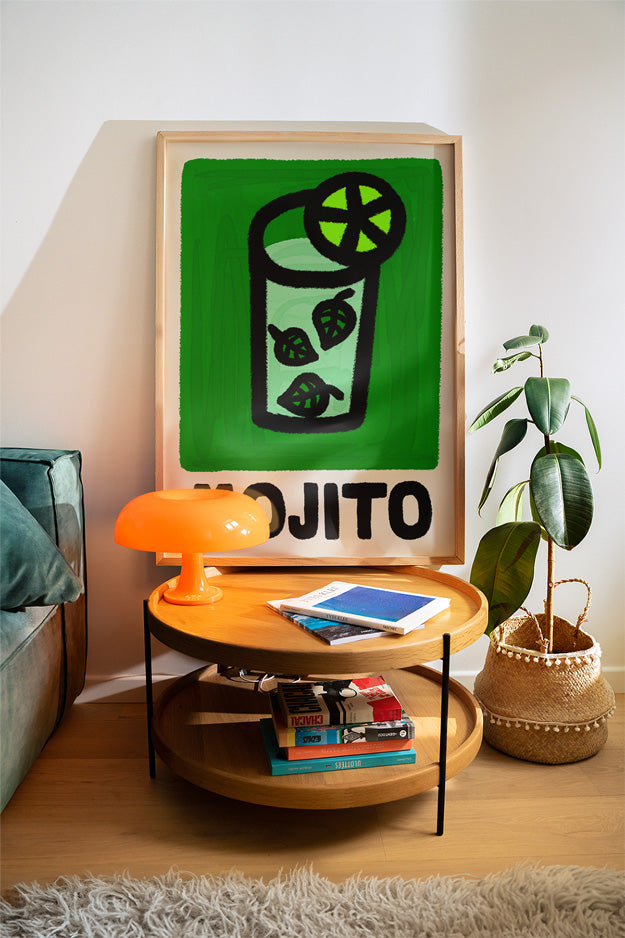 Living room with a round wooden table, lamp, books, and a framed mojito cocktail artwork of a mojito.