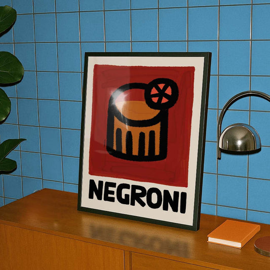 Framed Negroni cocktail poster on a wooden cabinet against a blue tiled wall.